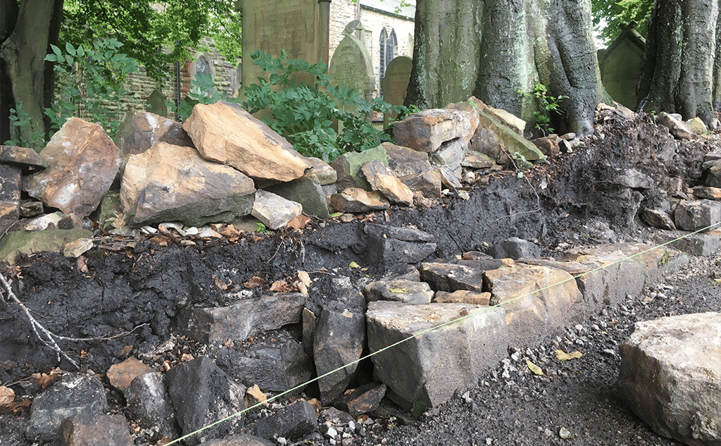 Gritstone dry stone wall with mortared half-round copestones for churchyard boundary wall