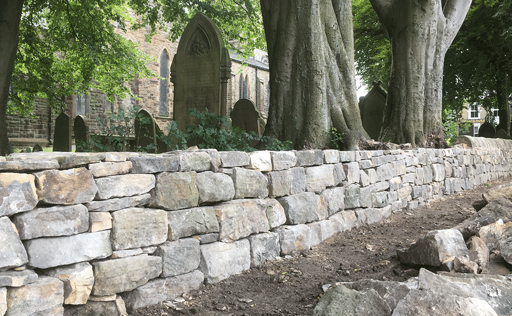 Gritstone dry stone wall with mortared half-round copestones for churchyard boundary wall